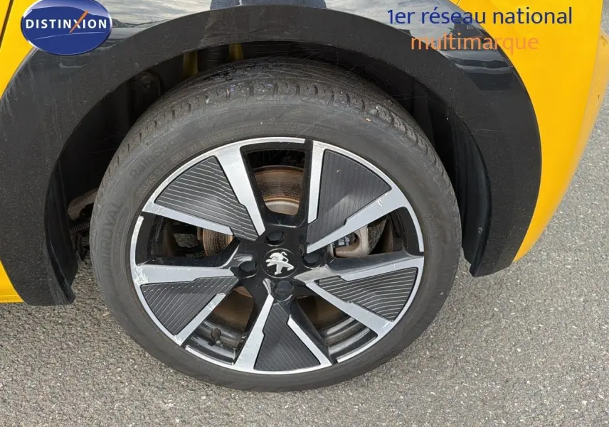 Gros plan sur la roue avant droite d'une Peugeot 208 électrique jaune Faro métal avec jante noire et argentée.
