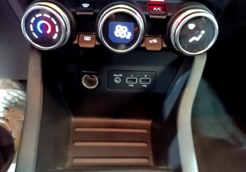 Gros plan sur la console centrale de la Renault Clio Business E-TECH 140, avec commandes de climatisation et ports USB visibles.