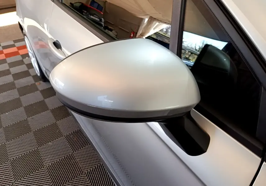 Gros plan sur le rétroviseur droit gris clair de la Renault Clio Business E-TECH 140, avec partie de la porte blanche visible.