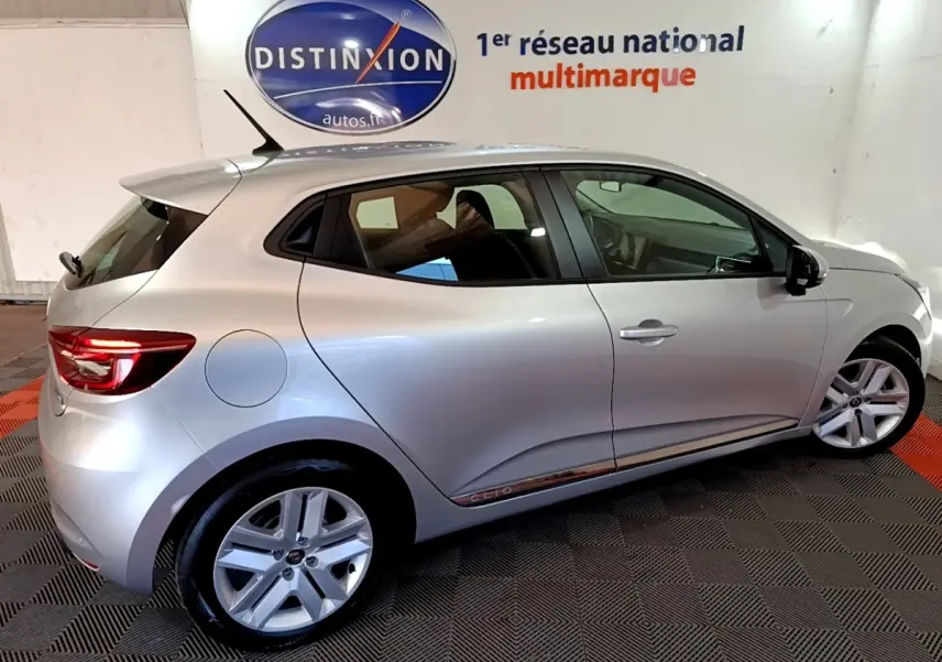 Vue latérale droite d'une Renault Clio gris clair 5 portes en intérieur sur sol damier noir et rouge.