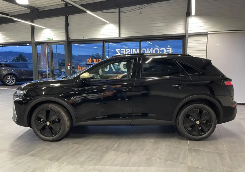 Vue de profil côté gauche du DS7 Crossback noir métallisé avec jantes noires et calandre discrète en intérieur showroom.