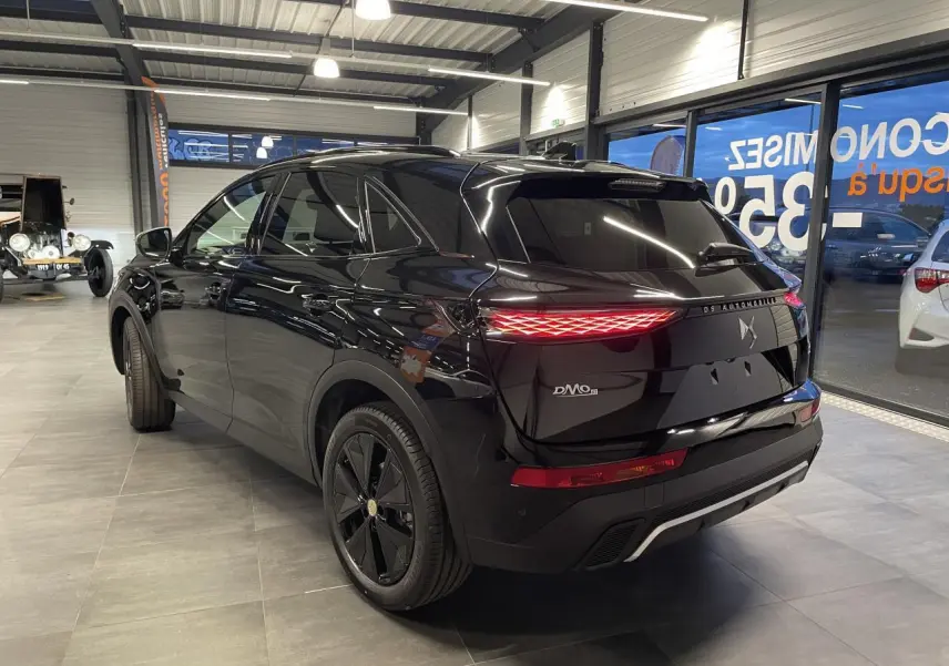 Vue 3/4 arrière droite du DS7 Crossback noir métallisé avec feux arrière DS Pixel LED allumés en intérieur showroom.
