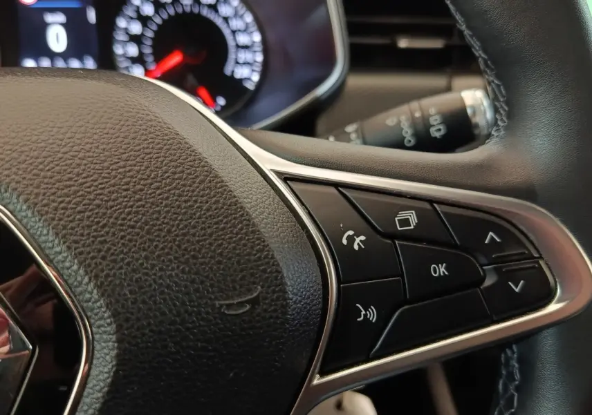 Gros plan sur le volant cuir synthétique de la Renault Clio Business blanc, avec commandes multifonctions et tableau de bord en arrière-plan.