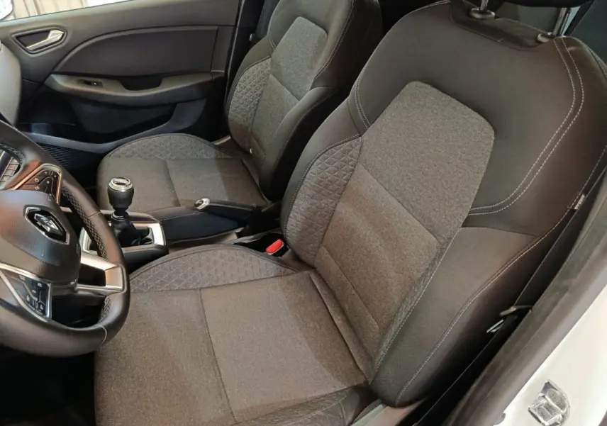 Vue intérieure côté conducteur de la Renault Clio Business blanche 2021, sièges tissu gris et volant cuir multifonctions.