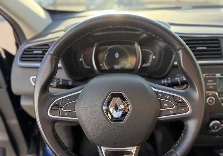 Vue rapprochée du volant en cuir noir avec commandes intégrées du Renault Kadjar 2019, tableau de bord numérique en arrière-plan.