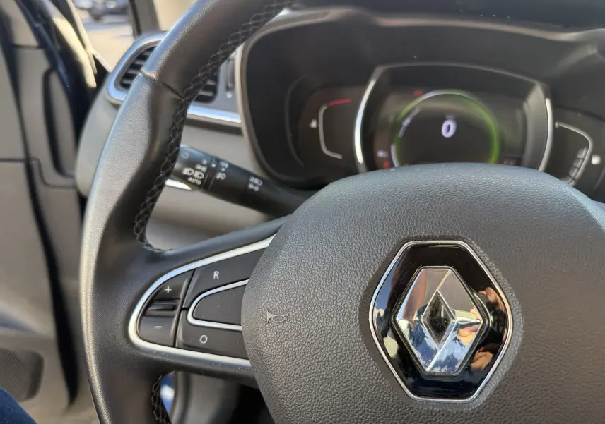 Vue rapprochée du volant noir avec logo Renault du Renault Kadjar bleu, tableau de bord numérique en arrière-plan.