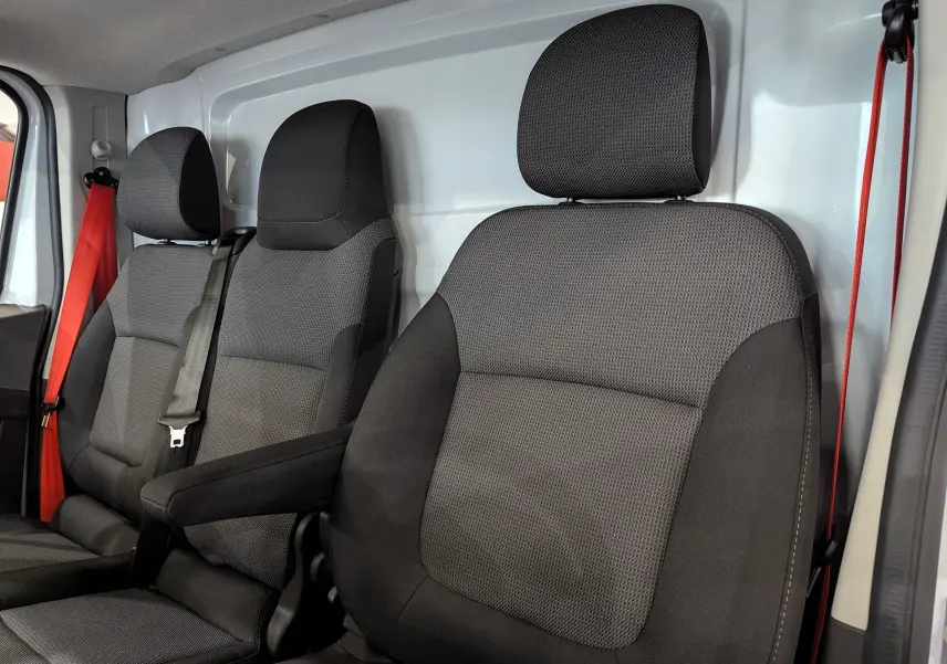 Vue intérieure des sièges avant noirs en tissu du Renault Trafic Fourgon blanc, avec ceinture rouge visible côté gauche.
