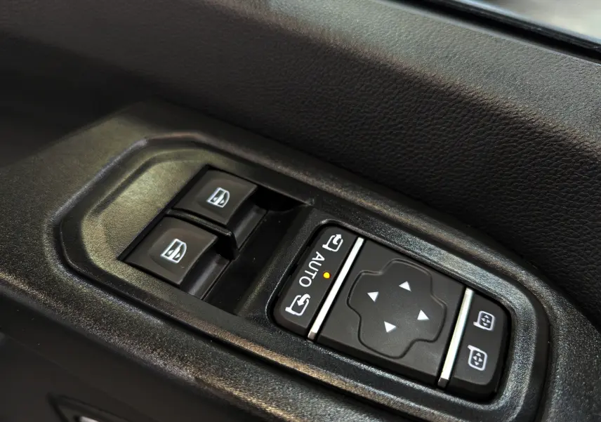 Gros plan sur les commandes de lève-vitres et réglage des rétroviseurs côté gauche du Renault Trafic Fourgon blanc 2025.