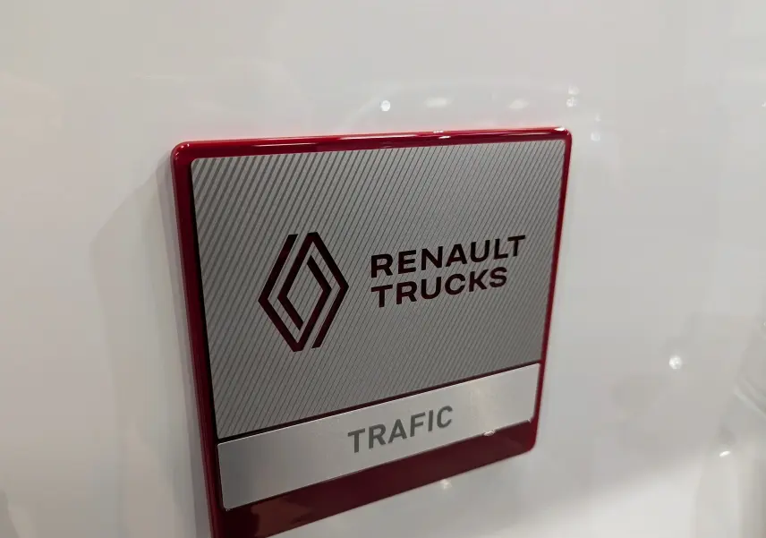 Gros plan sur l'écusson Renault Trucks rouge et gris sur la carrosserie blanche du Trafic Fourgon L2H1.
