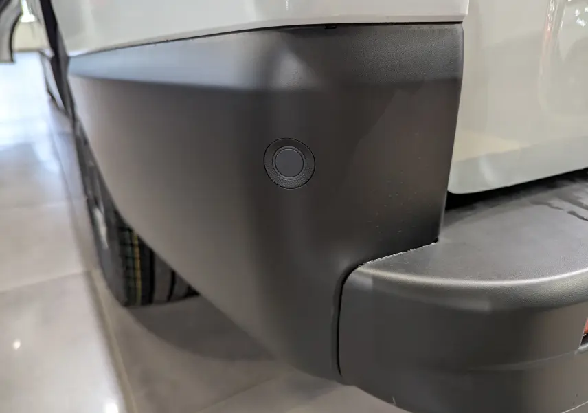 Gros plan sur le pare-chocs arrière noir du Renault Trafic Fourgon blanc minéral, avec capteur de recul circulaire visible.