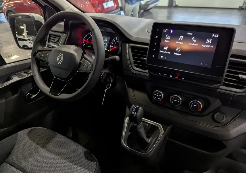 Vue intérieure côté conducteur du Renault Trafic Fourgon blanc, mettant en valeur le volant multifonction et l'écran tactile central.