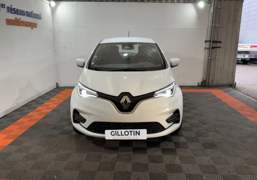 Vue frontale d'une Renault ZOE blanche 2020 avec phares LED allumés dans un garage.