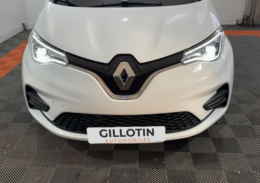 Vue frontale rapprochée de la Renault ZOE Business blanche avec phares LED allumés et logo Renault bien visible.