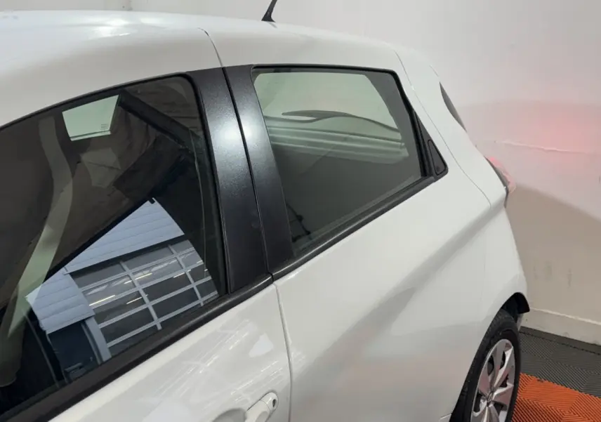Vue côté gauche arrière d'une Renault ZOE Business blanche, mettant en valeur la vitre arrière et la poignée de porte.