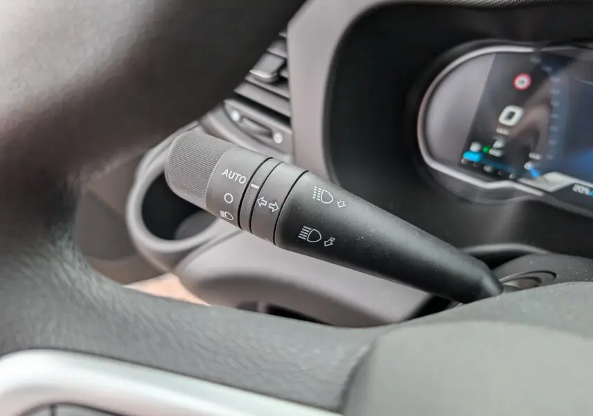 Gros plan sur le commodo noir des phares et clignotants à gauche du volant dans l'habitacle du Iveco Daily blanc.