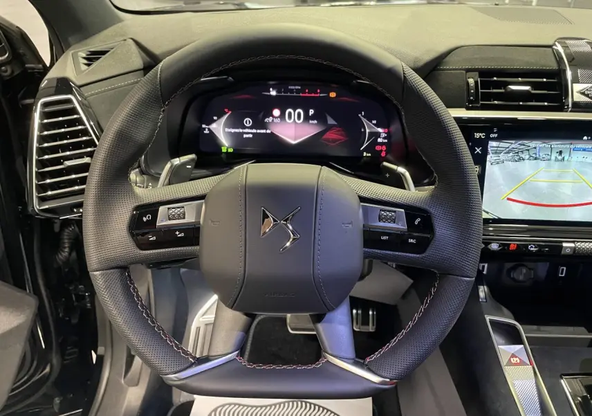 Vue intérieure centrée sur le volant DS en cuir noir perforé avec surpiqûres rouges et tableau de bord numérique allumé.