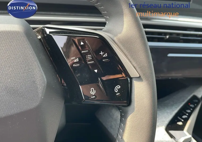 Gros plan sur les commandes gauche du volant cuir noir du Peugeot 3008 Hybrid gris Artense, avec tableau de bord en arrière-plan.