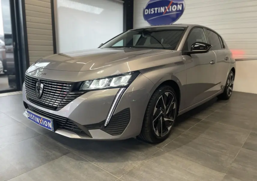 Peugeot 308 gris Artense vue 3/4 avant droit en showroom avec calandre noire et feux LED distinctifs.