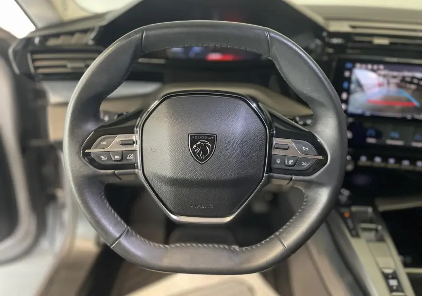 Volant en cuir noir de la Peugeot 308 2022 avec commandes intégrées et écran tactile affichant la caméra de recul.