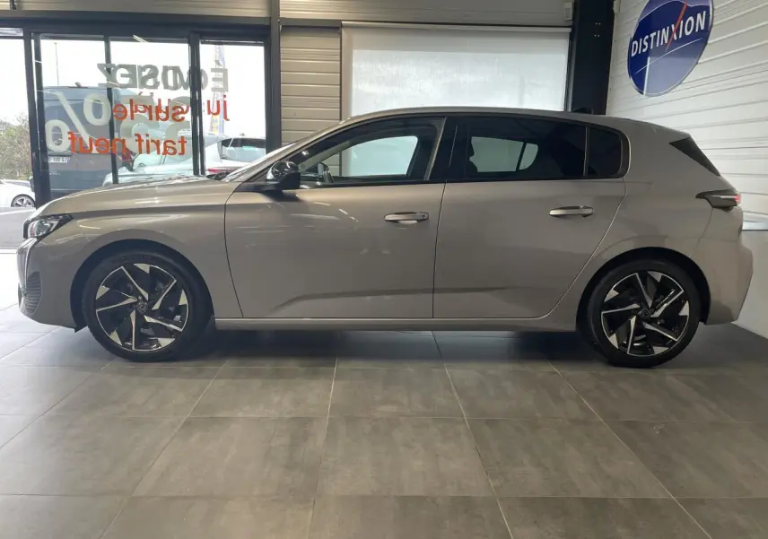 Profil côté gauche de la Peugeot 308 gris Artense 2022 avec jantes alliage 17'' et vitres surteintées en showroom.
