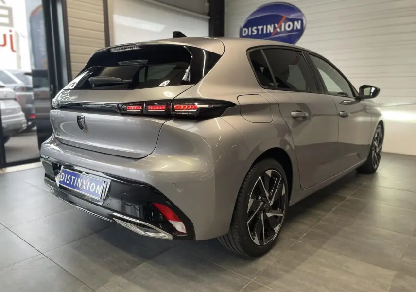 Vue 3/4 arrière droit d'une Peugeot 308 gris Artense avec feux arrière LED et jantes alliage 17 pouces en showroom.