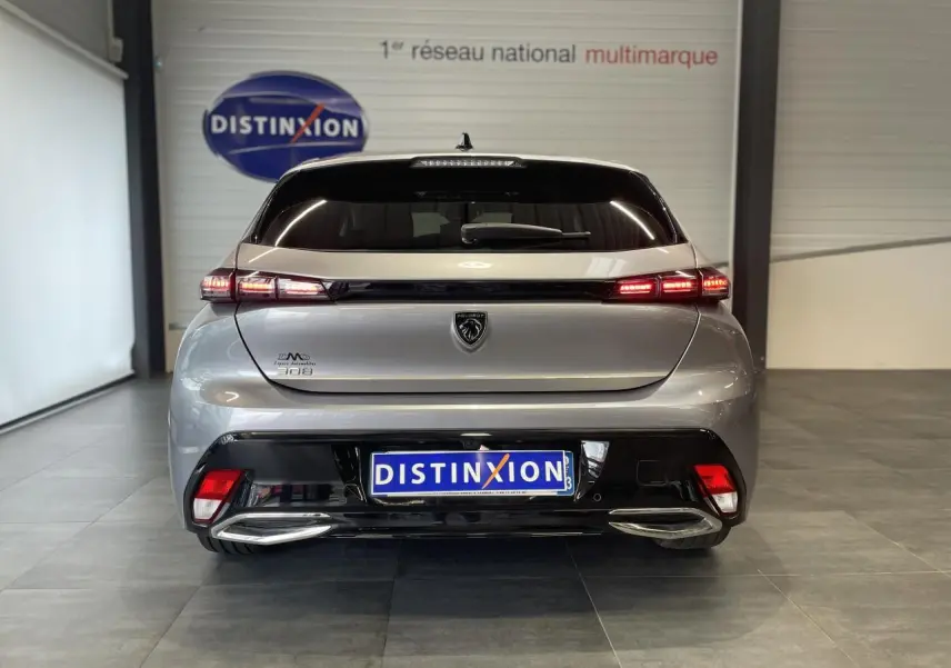 Vue arrière d'une Peugeot 308 gris Artense avec feux LED allumés et double sortie d'échappement chromée dans un showroom.