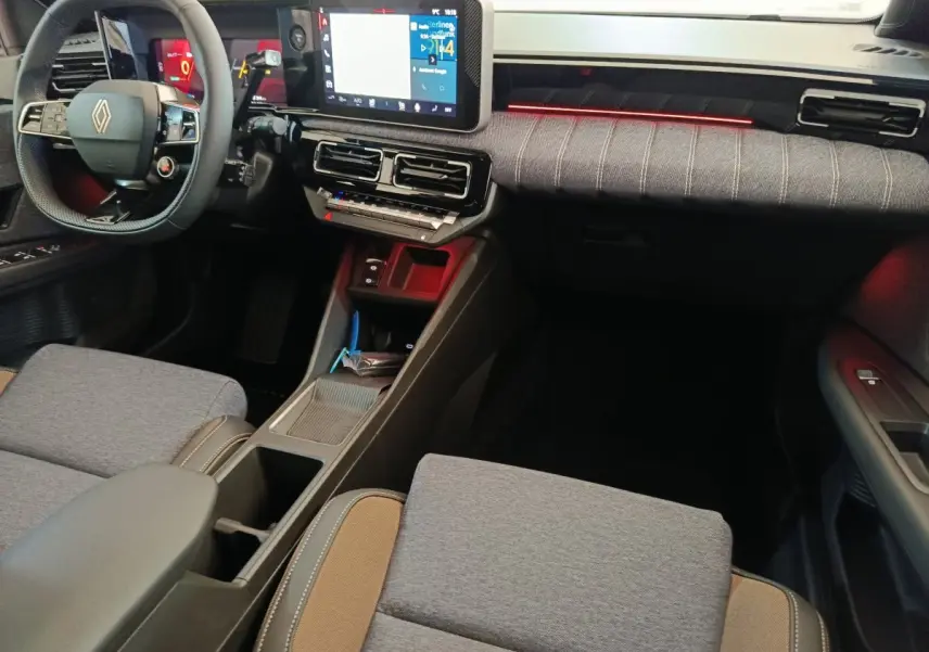 Vue intérieure avant droite de la Renault R5 Techno 150 ch 2025, avec tableau de bord tactile et éclairage d'ambiance rouge.