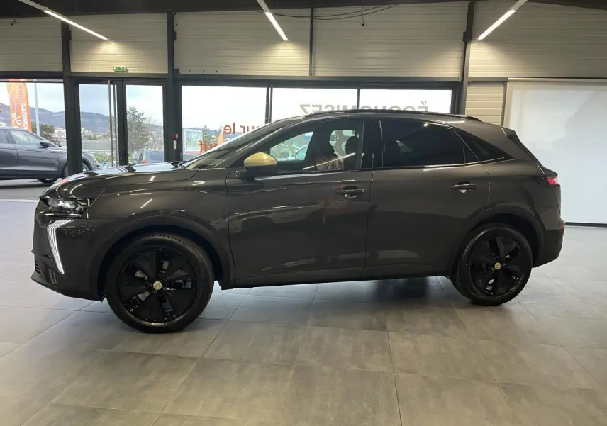 Vue latérale droite du DS7 Crossback gris titanium avec jantes noires et rétroviseurs dorés satinés en intérieur showroom.