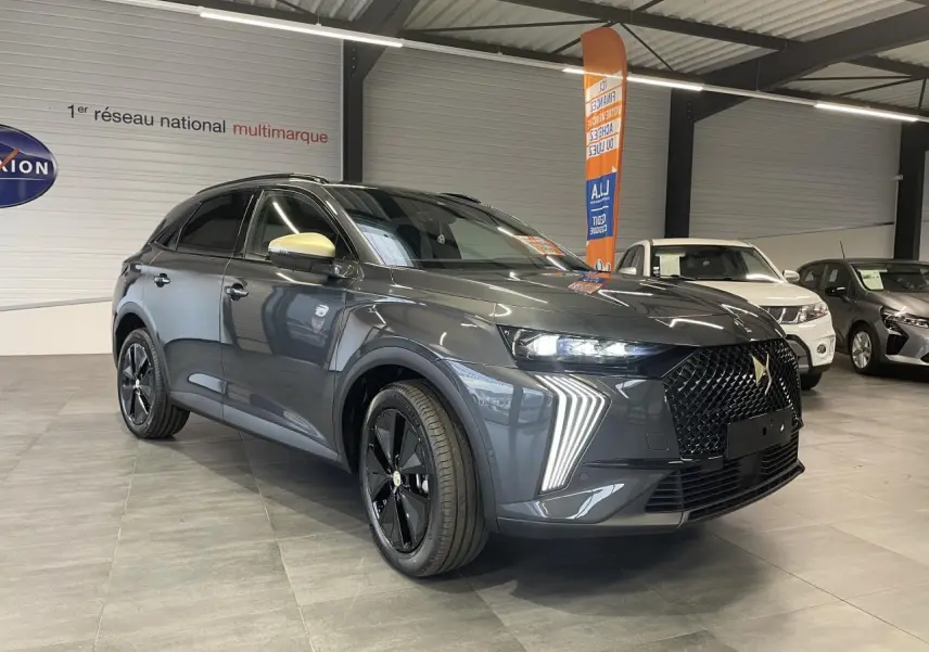 Vue 3/4 avant du DS7 Crossback gris titanium avec calandre noire et coques de rétroviseurs dorées satinées en showroom.