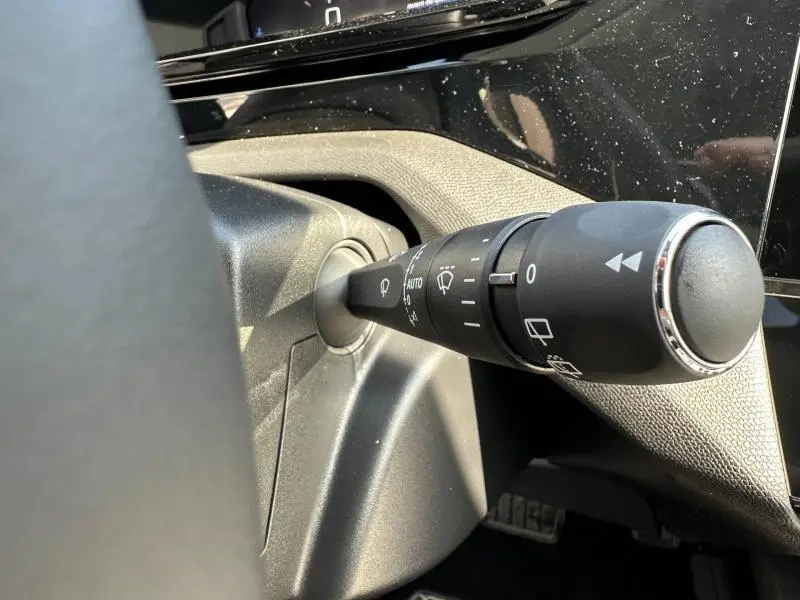 Gros plan sur la commande des essuie-glaces à gauche du volant dans l'habitacle noir du Peugeot 308 bleu 2025.