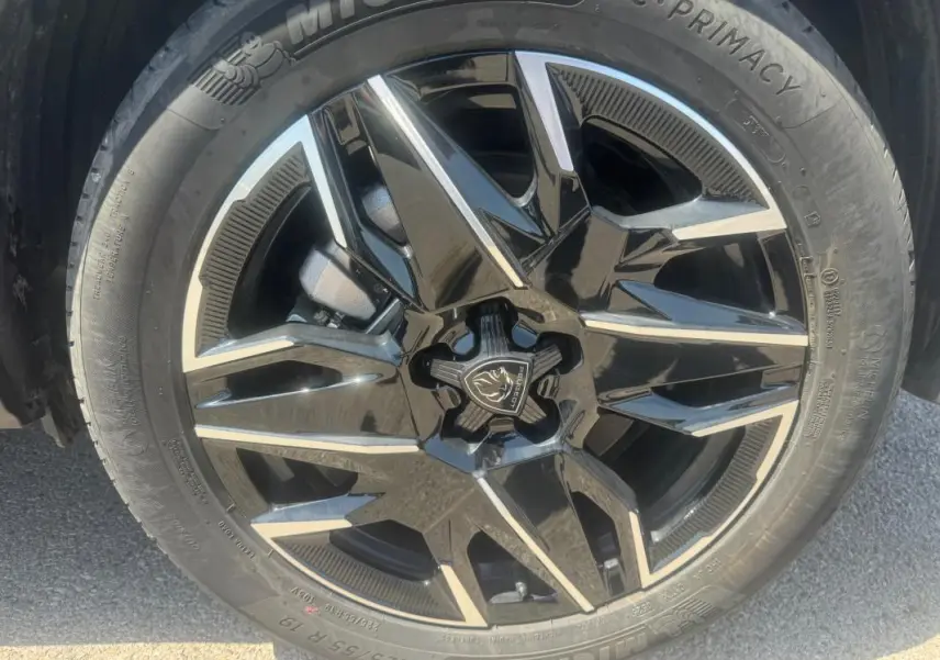 Gros plan sur la jante noire et argentée d’un Peugeot 5008 Hybrid gris, mettant en valeur le logo central et le pneu Michelin.