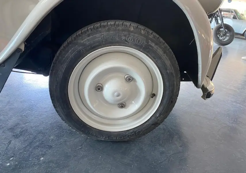 Gros plan sur la roue arrière droite beige clair d'une Citroën 2 CV 1968 refaite à neuf, avec jante métallique simple.