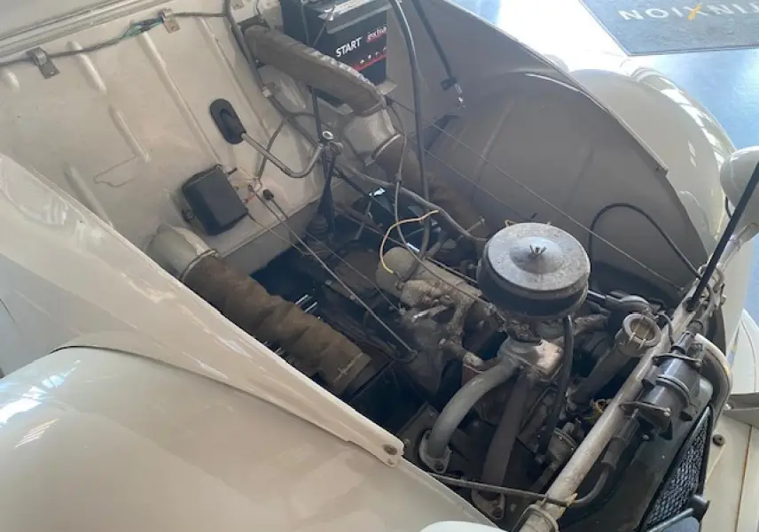 Moteur visible sous le capot ouvert d'une Citroën 2 CV beige clair refaite à neuf, vue de trois quarts avant droit.