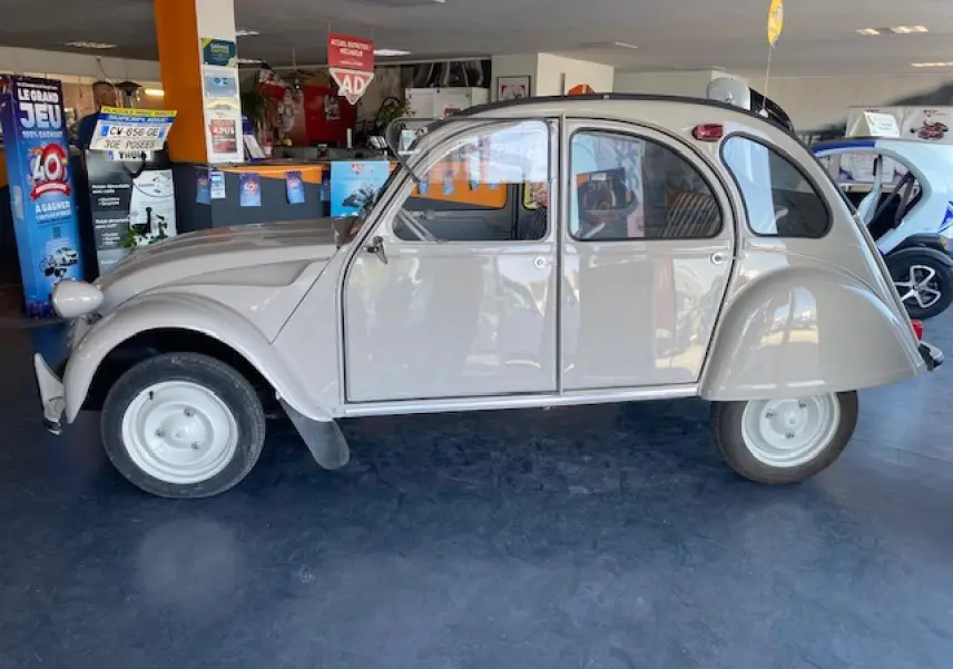 Profil côté gauche d'une Citroën 2 CV beige clair refaite à neuf, exposée en intérieur avec ses formes arrondies classiques.