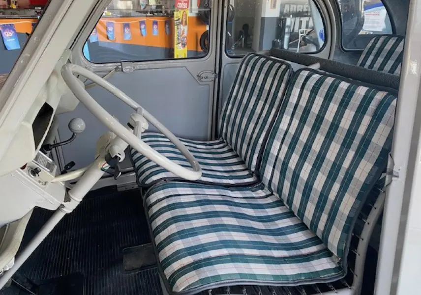 Intérieur de la Citroën 2 CV beige clair de 1968, vue côté conducteur montrant le volant et les sièges à motifs rayés.