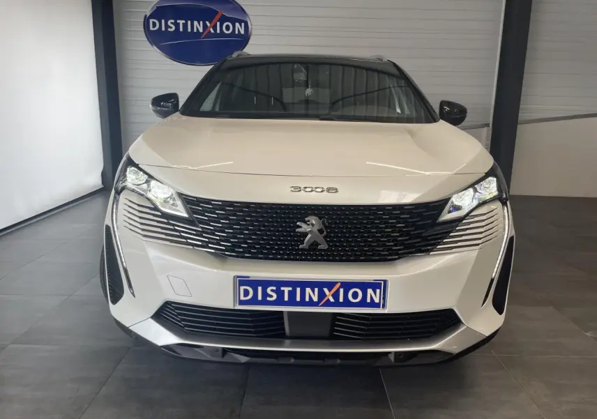 Vue frontale d'un Peugeot 3008 blanc nacré avec calandre noire et phares LED allumés en intérieur showroom.