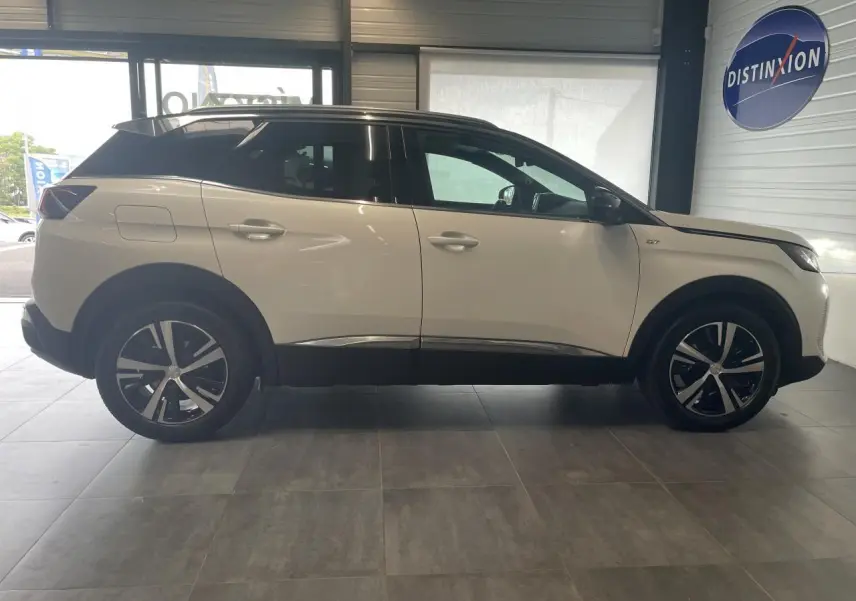 Profil droit du Peugeot 3008 GT blanc nacré avec toit noir et jantes alliage bi-ton dans un showroom.