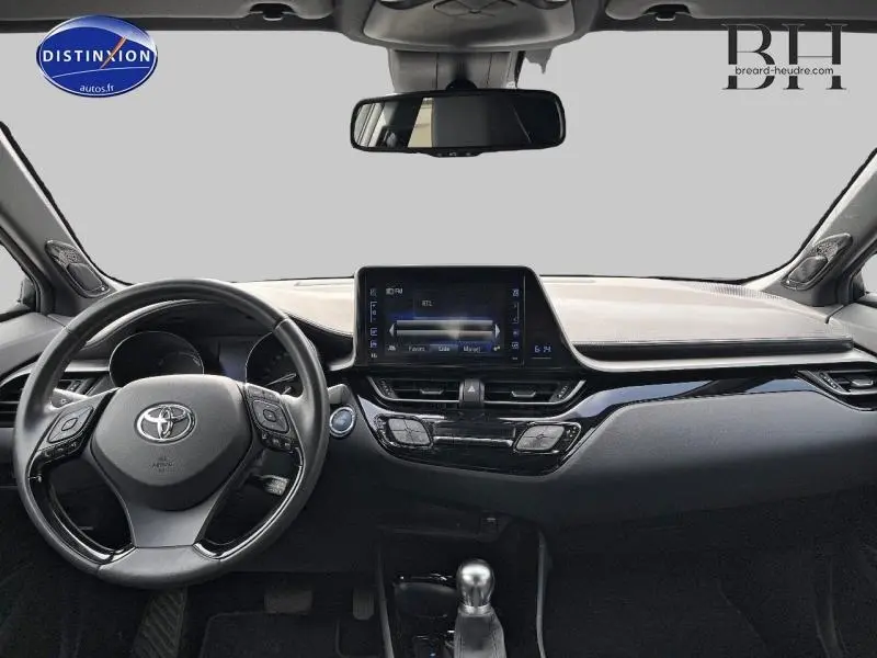 Vue intérieure du tableau de bord et volant cuir multifonction du Toyota C-HR blanc nacré 2019 avec écran tactile central.