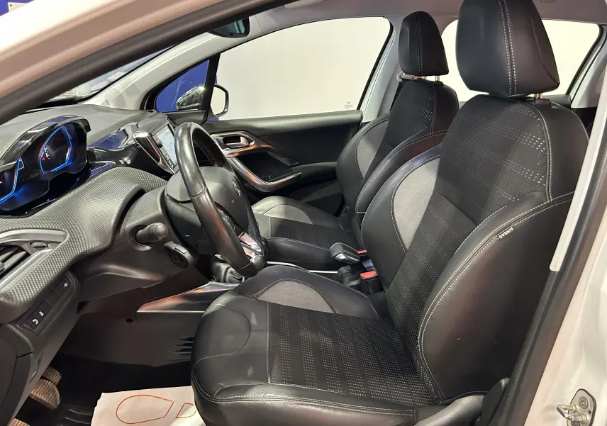Intérieur avant du Peugeot 2008 blanc, vue côté gauche, sièges cuir noirs avec coutures blanches et tableau de bord moderne.