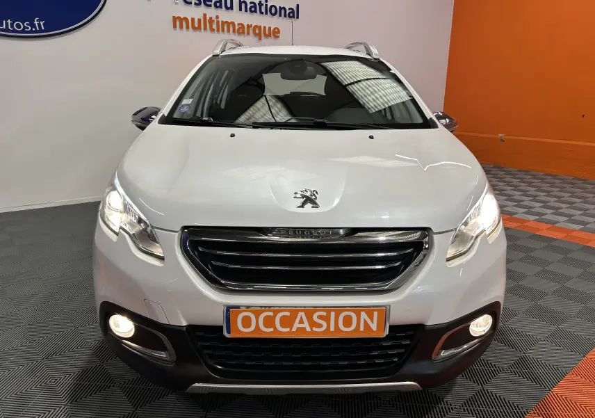 Vue avant d'un Peugeot 2008 blanc de 2014 avec phares allumés et plaque "OCCASION" en intérieur showroom.
