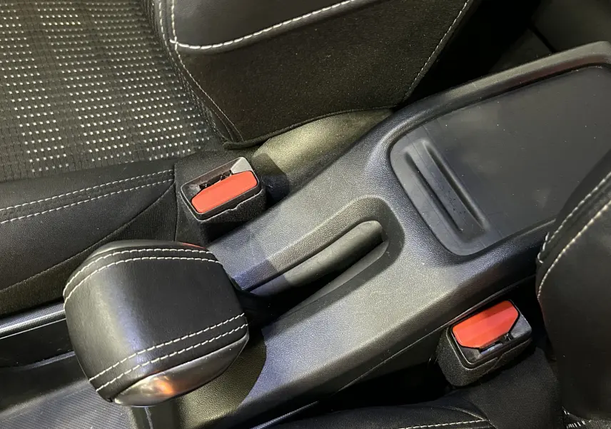 Gros plan sur le frein à main en cuir noir et les boucles de ceinture rouge dans l'habitacle d'une Peugeot 2008 blanche.