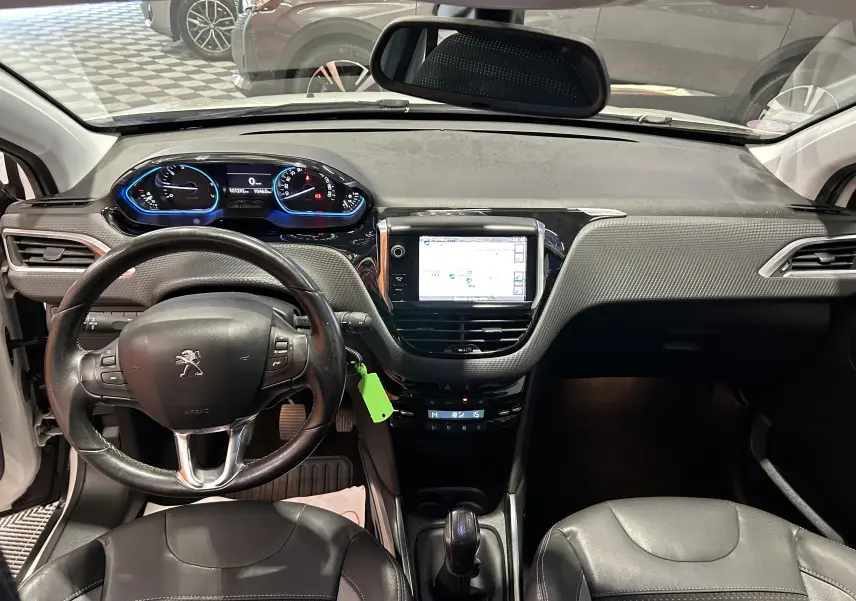 Vue intérieure avant du tableau de bord de la Peugeot 2008 blanc, avec volant cuir et écran GPS central allumé.