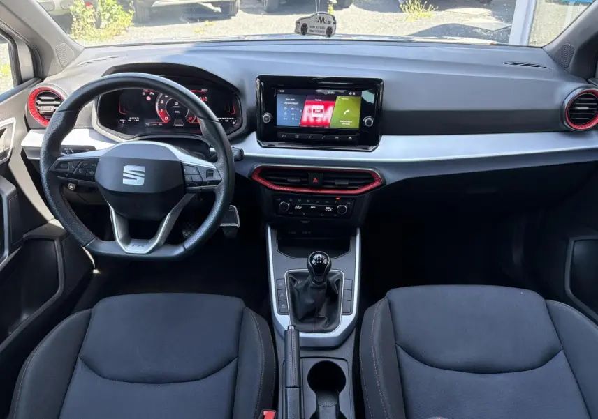 Vue intérieure avant du tableau de bord et volant cuir de la SEAT Arona 2024 avec écran tactile et détails rouges sur aérateurs.