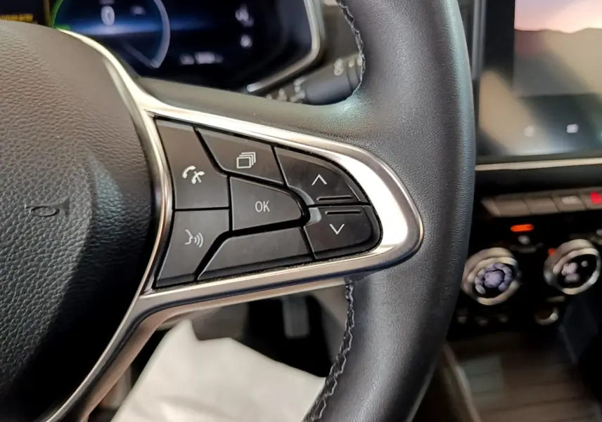 Gros plan sur les commandes multifonctions côté droit du volant cuir noir de la Renault ZOE blanche, tableau de bord en arrière-plan flou.