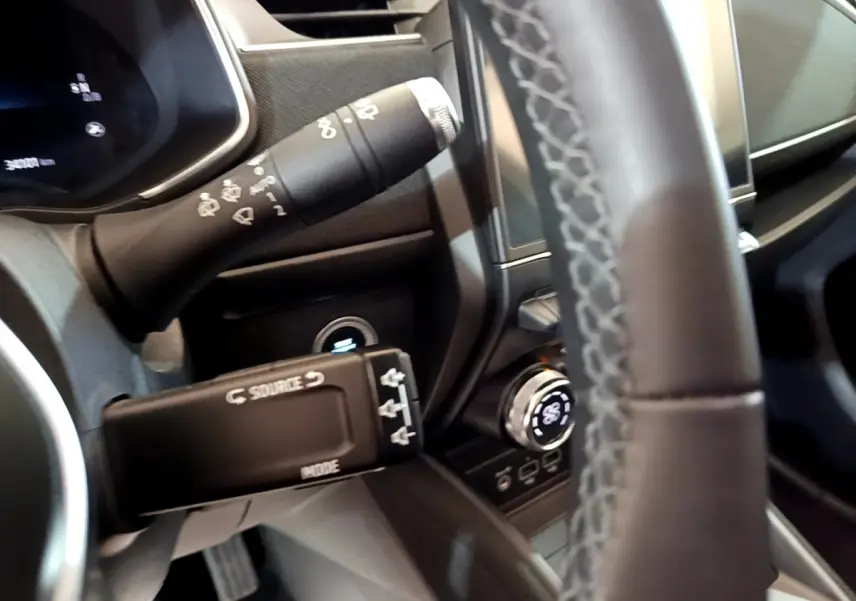 Gros plan sur la commande multifonction et le volant en cuir synthétique côté gauche du tableau de bord de la Renault ZOE blanche.