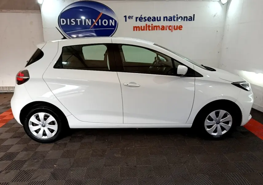 Profil droit d'une Renault ZOE Business R110 blanche de 2021, compacte et électrique, en intérieur sur sol damier noir et rouge.