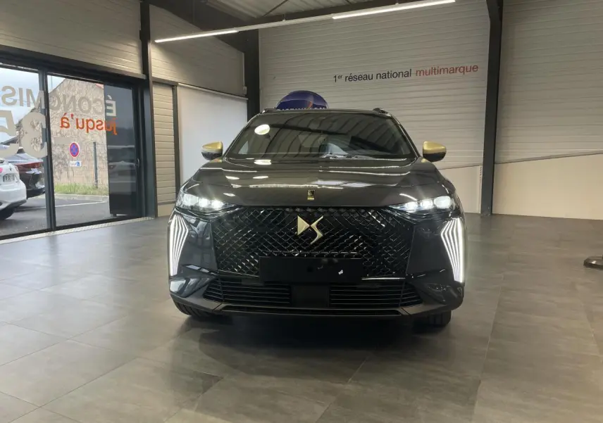 Vue de face du DS7 Crossback gris titanium avec calandre noire brillante et feux LED verticaux allumés en showroom.