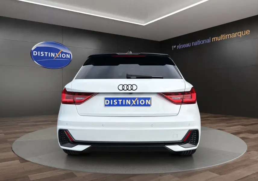Vue arrière d'une Audi A1 Sportback blanche avec toit noir, feux LED et diffuseur arrière noir en showroom.