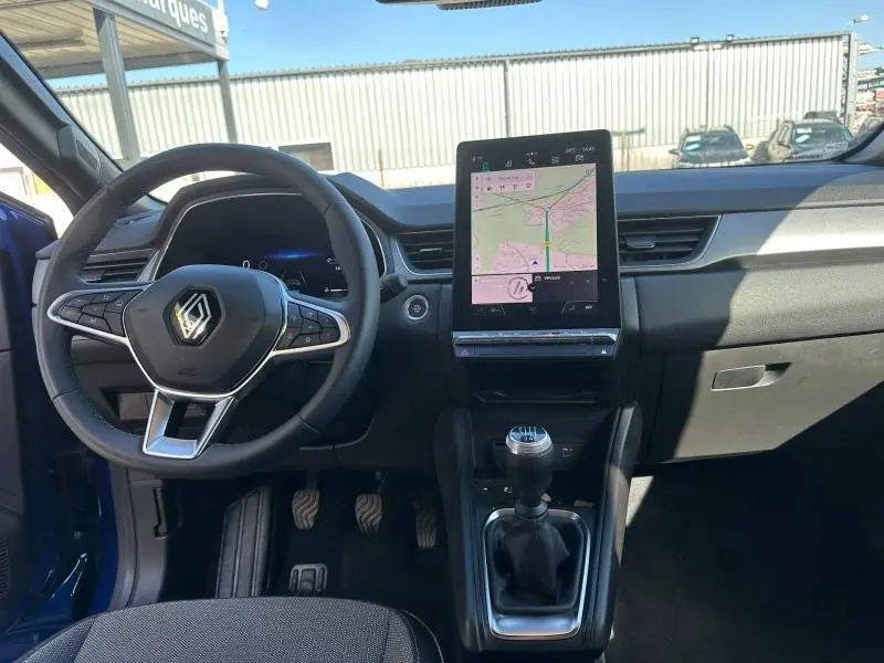 Vue intérieure frontale du Renault Captur 2025, tableau de bord noir avec écran tactile vertical et levier de vitesses manuel.