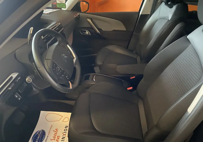 Intérieur avant du Citroën Grand C4 Spacetourer 2022, sièges noirs en tissu et cuir, volant multifonction visible côté conducteur.